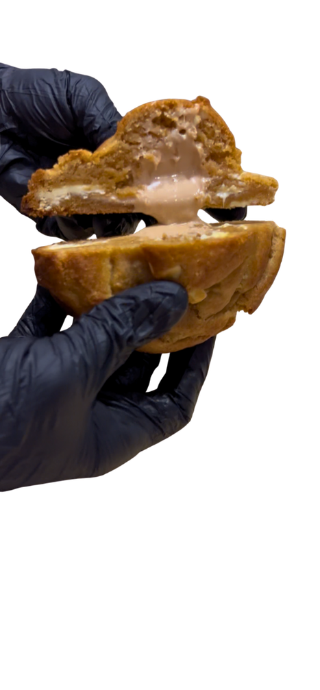 Black-gloved hands pulling apart a large cookie, showing its soft centre